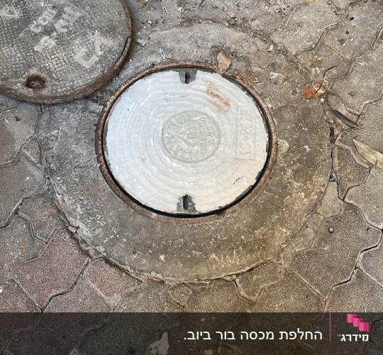 מכסה ביוב על מדרכה עם לכלוך מסביב